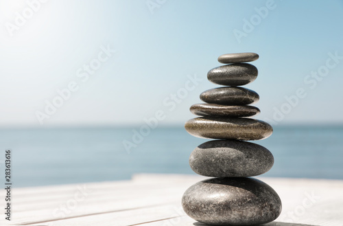 Stack of stones on wooden pier near sea, space for text. Zen concept