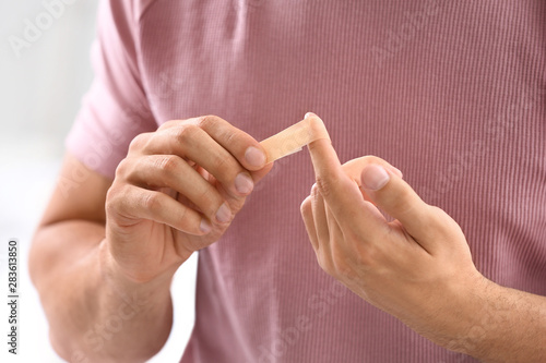 Man applying adhesive bandage on finger, closeup view