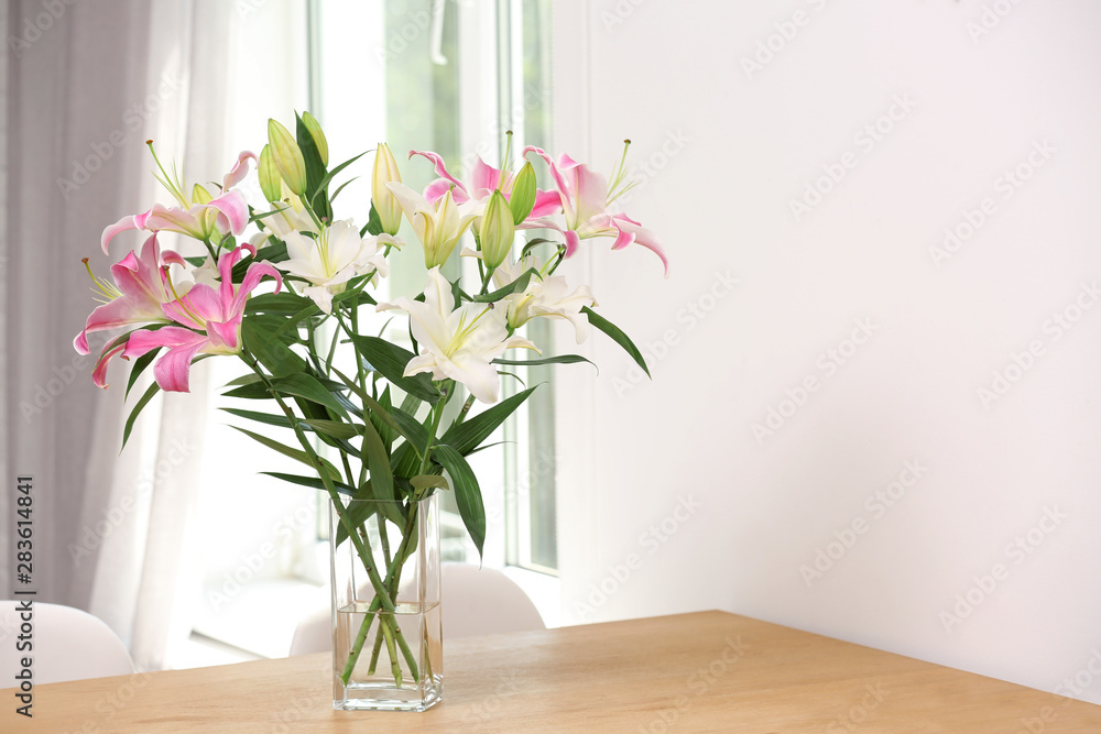 Vase with bouquet of beautiful lilies on wooden table indoors. Space for text Vase with bouquet of beautiful lilies on wooden table indoors. Space for text
