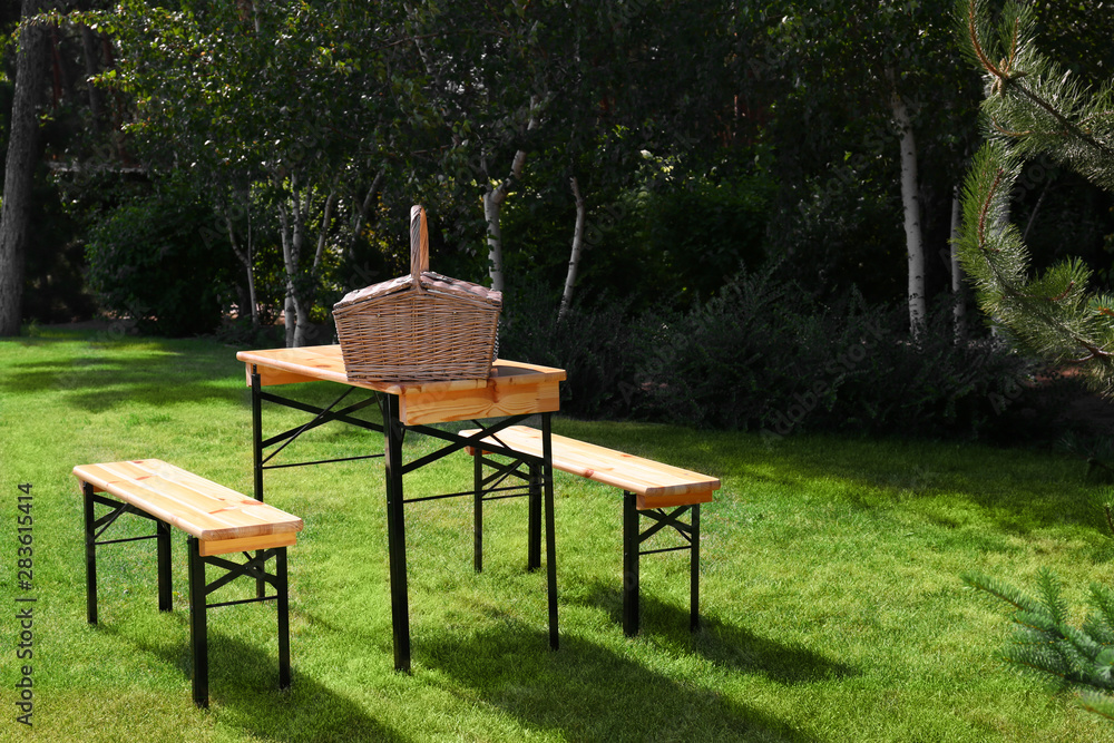 Picnic basket on wooden table in green park. Space for text Picnic basket on wooden table in green park. Space for text