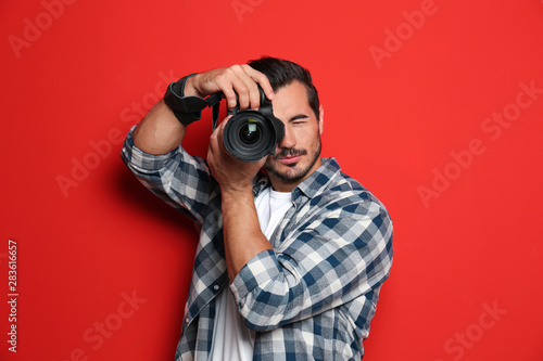 Young professional photographer taking picture on red background photo