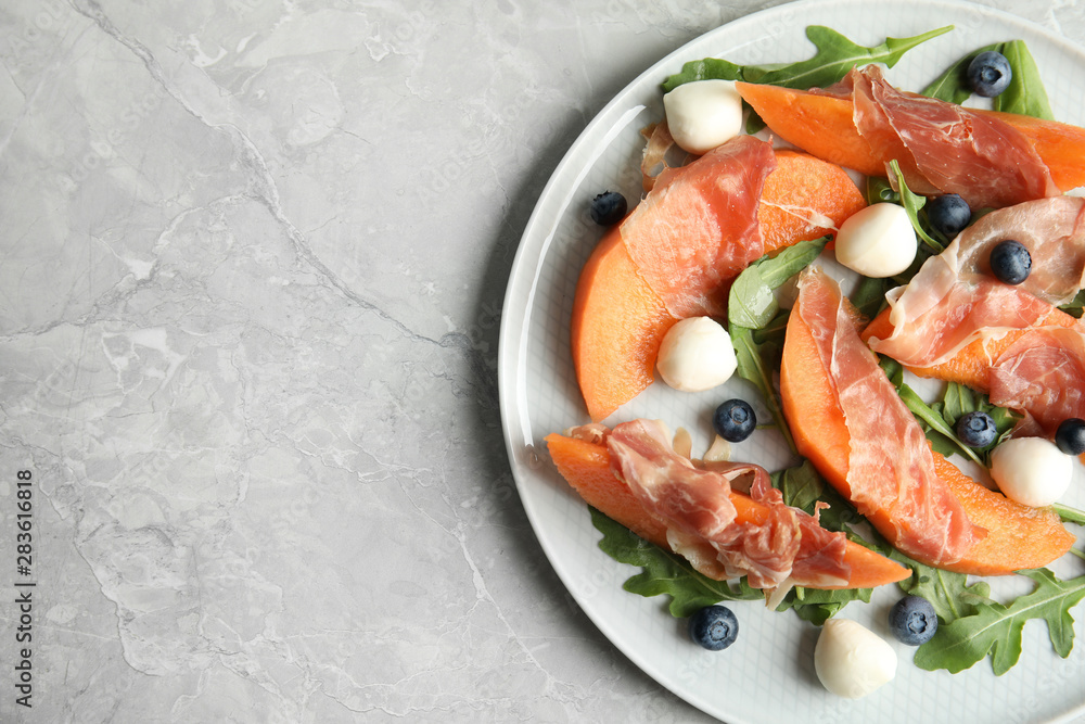 Fresh melon with prosciutto, mozzarella and arugula on light grey table, above view. Space for text Fresh melon with prosciutto, mozzarella and arugula on light grey table, above view. Space for text