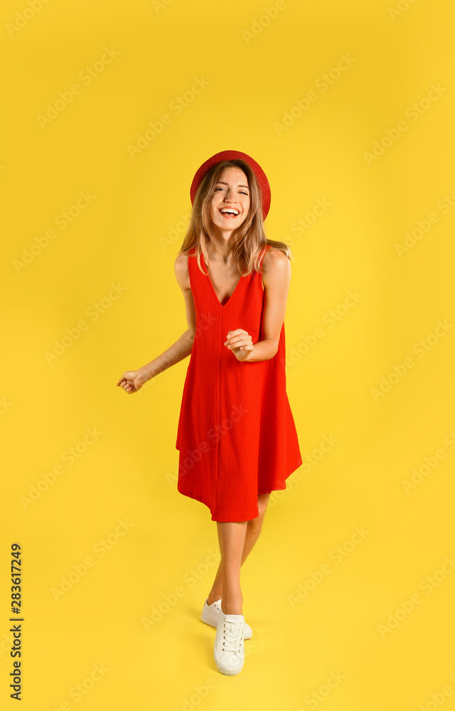 Beautiful young woman in red dress dancing on yellow background