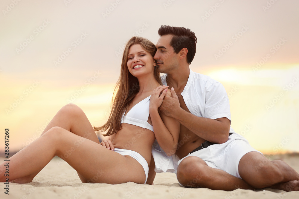 Happy young couple relaxing together on sea beach at sunset