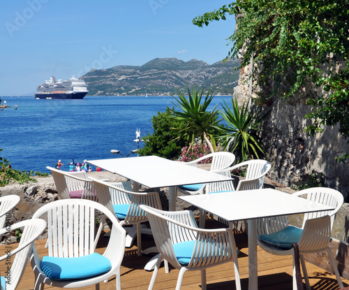 close-up of white tables and chairs on the terrace overlooking the blue Adriatic sea on which the cruise ship sails.