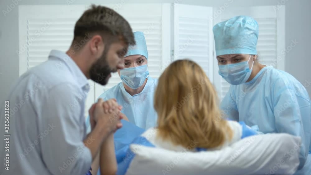 Husband and nurses supporting pregnant woman hardly breathing during child birth Husband and nurses supporting pregnant woman hardly breathing during child birth