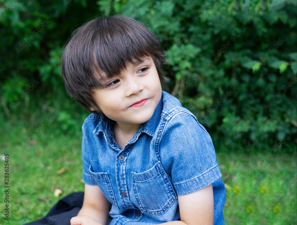 Portrait of a young boy sitting on lawn in the park, Active child looking out with smiling face sitting on green grass field, Kid having fun playing outdoors in sunny day summer, Portrait of a young boy sitting on lawn in the park, Active child looking out with smiling face sitting on green grass field, Kid having fun playing outdoors in sunny day summer,