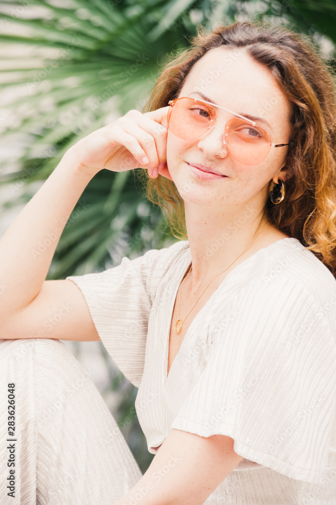 Millenial trendy Hipster teenager enjoys and relaxes during a walk in city center, she has orange lens glasses and white minimalistic dress, portraiture series,