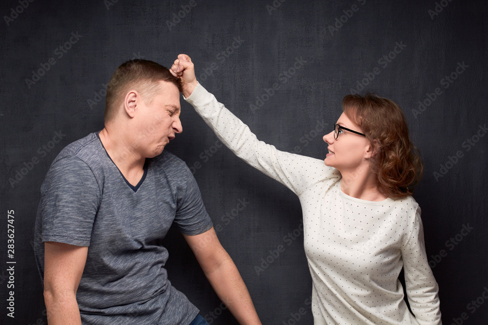 Enraged woman is beating man wincing and crouching from pain Enraged woman is beating man wincing and crouching from pain