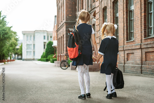 Back to school, Portrait from the back of elementary school students with backpacks in uniform holding hands. In the background of an old building education.