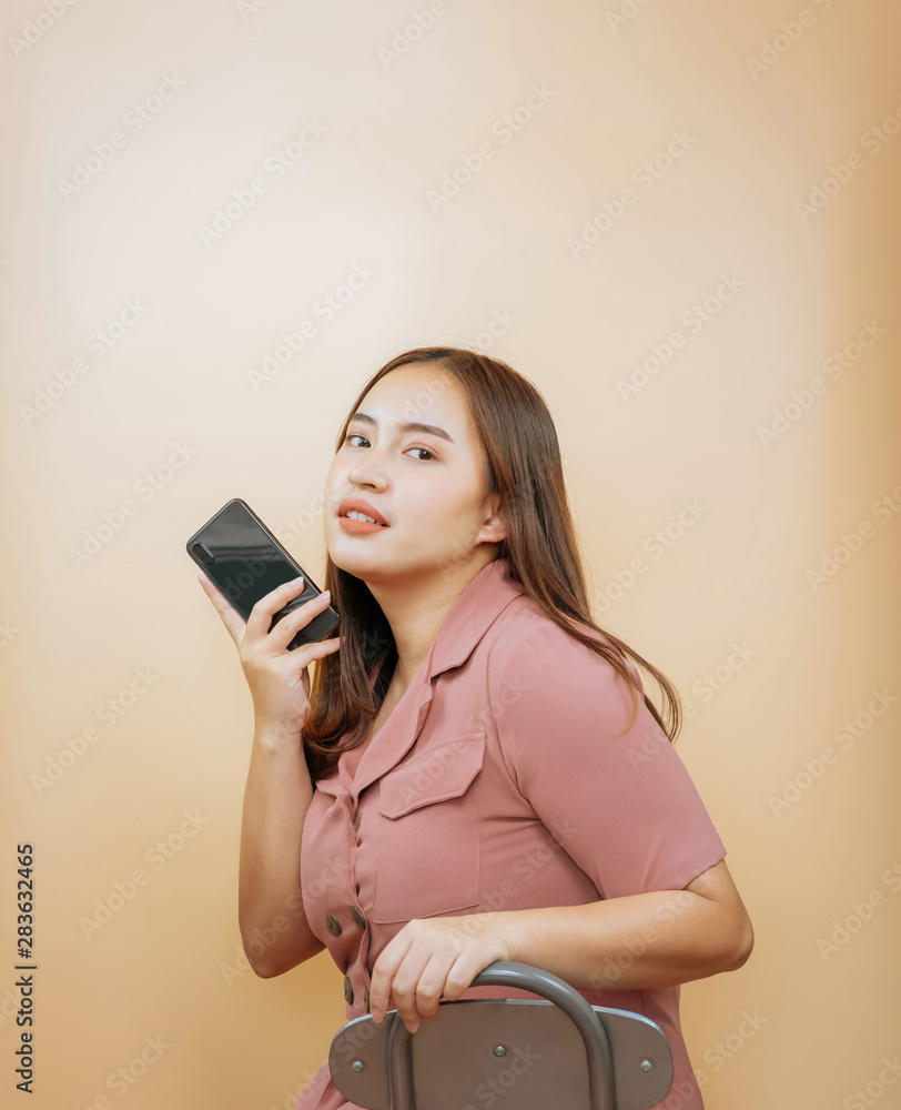 Naklejka premium Asian woman sitting on the chair holding smartphone on orange background. copy space for put advertisement.