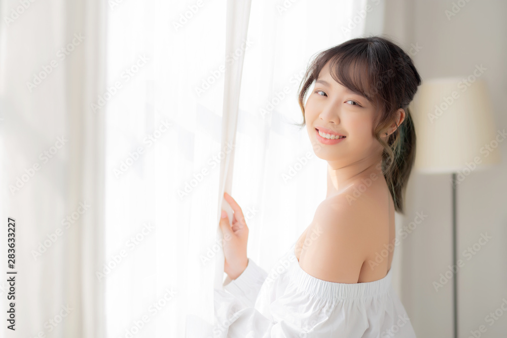 Portrait of beautiful young asian woman standing the window and smile while wake up with sunrise at morning, girl happy with freshness and cheerful, lifestyle and relax concept. Portrait of beautiful young asian woman standing the window and smile while wake up with sunrise at morning, girl happy with freshness and cheerful, lifestyle and relax concept.