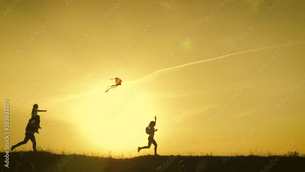 Happy family playing with a kite while on meadow, sunset, in summer day. Funny family time. Happy little girl launch a kite with parents. Mom, Dad and daughter are happy together. Happy family playing with a kite while on meadow, sunset, in summer day. Funny family time. Happy little girl launch a kite with parents. Mom, Dad and daughter are happy together.