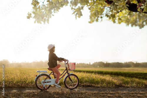 independent asian child ride her bicycle in countryside road by her self with beautiful scenery and sunset