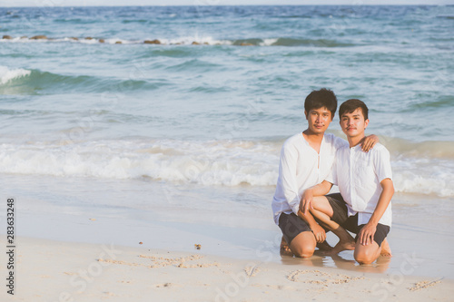 Young asian couple gay smiling romantic drawing word text love together on sand in vacation, homosexual happy and fun with love sitting on sand at the beach in travel summer, LGBT legal concept.