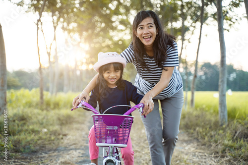 mom teach her toddler daughter to learn bicycle outdoor photo