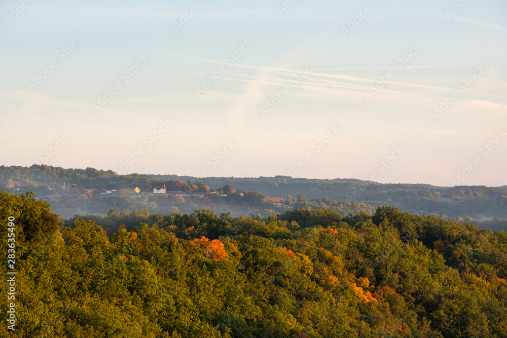 Morning mist rises over a dense forest in the Perigord region of France