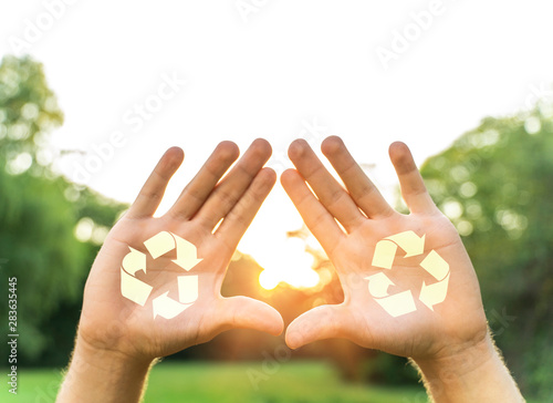 Recycle concept , man holding open hands with recycle symbol, sun rays in background 