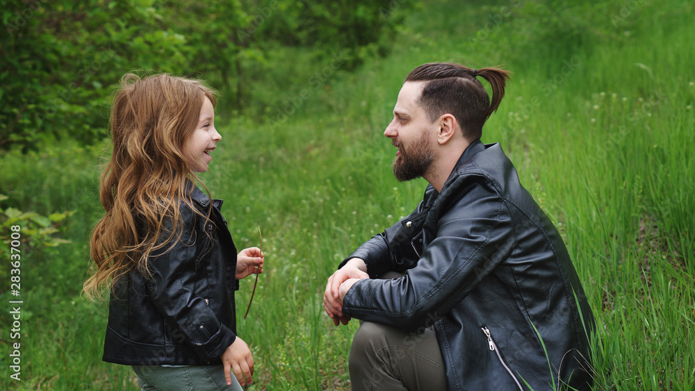 Modern stylish family walking in park. Daughter enjoys chatting with dad. Lovely moments spent to father in nature. Time together. Family look. Urban casual outfit. Trigger memories of childhood