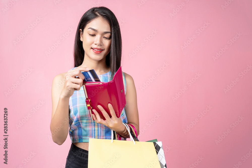 Fototapeta premium Young woman picking a credit card from her purse with smile and carrying shopping bags.