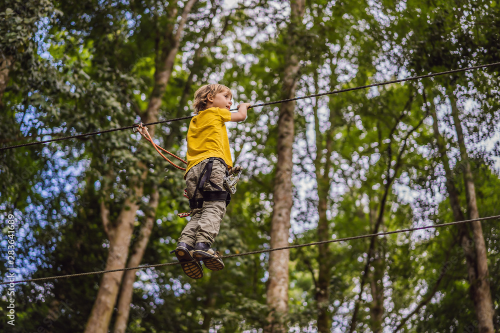 Little boy in a rope park. Active physical recreation of the child in the fresh air in the park. Training for children Little boy in a rope park. Active physical recreation of the child in the fresh air in the park. Training for children