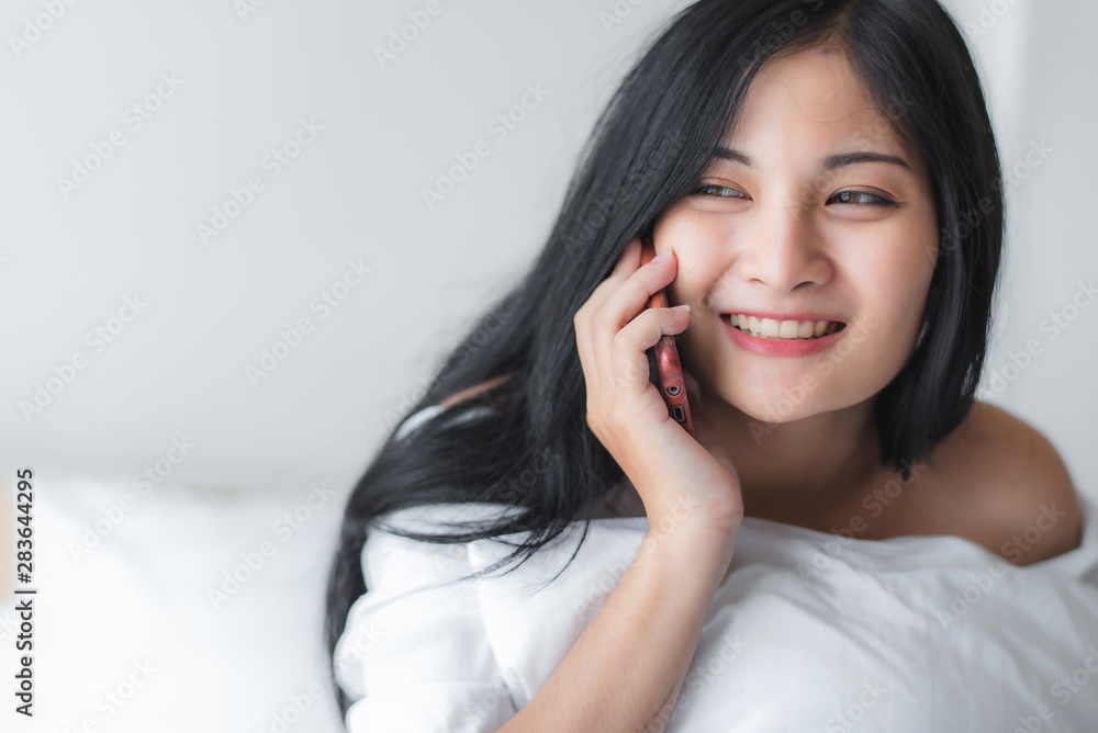 Beautiful attractive young Asian woman laying on bed and using smart phone or cellphone at bedroom in the morning. Beautiful attractive young Asian woman laying on bed and using smart phone or cellphone at bedroom in the morning.