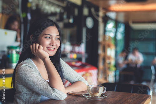 Beautiful attractive young Asian woman holding a cup of coffee in hand and sitting on sofa at cafe in the morning, vintage color tone.  © totojang1977