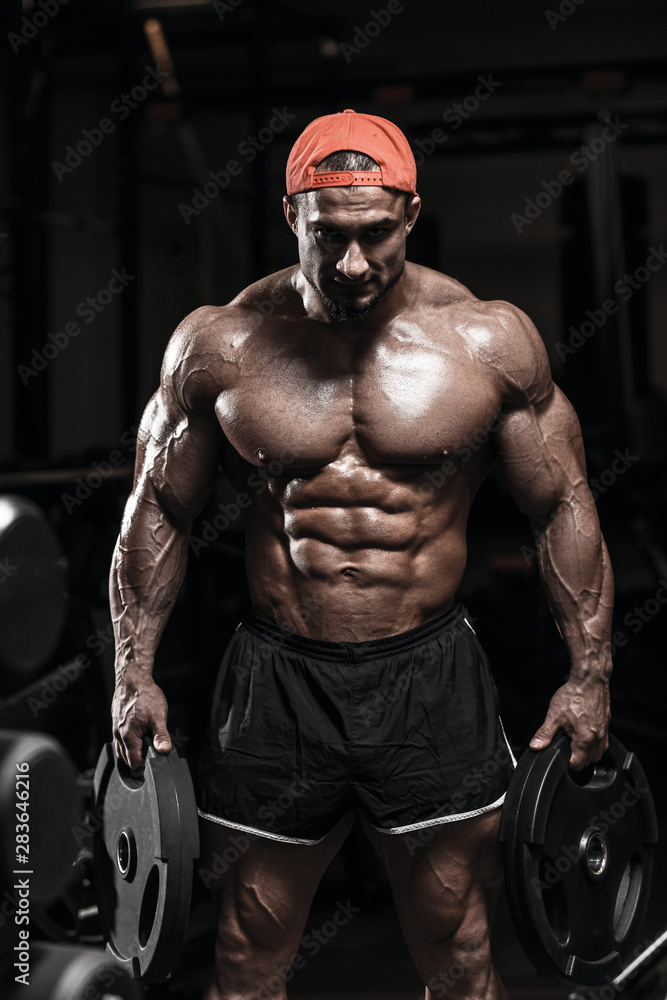 Muscular athletic bodybuilder man hard training in gym over dark background  with dramatic light with weights in strong pumped hands Stock Photo | Adobe  Stock