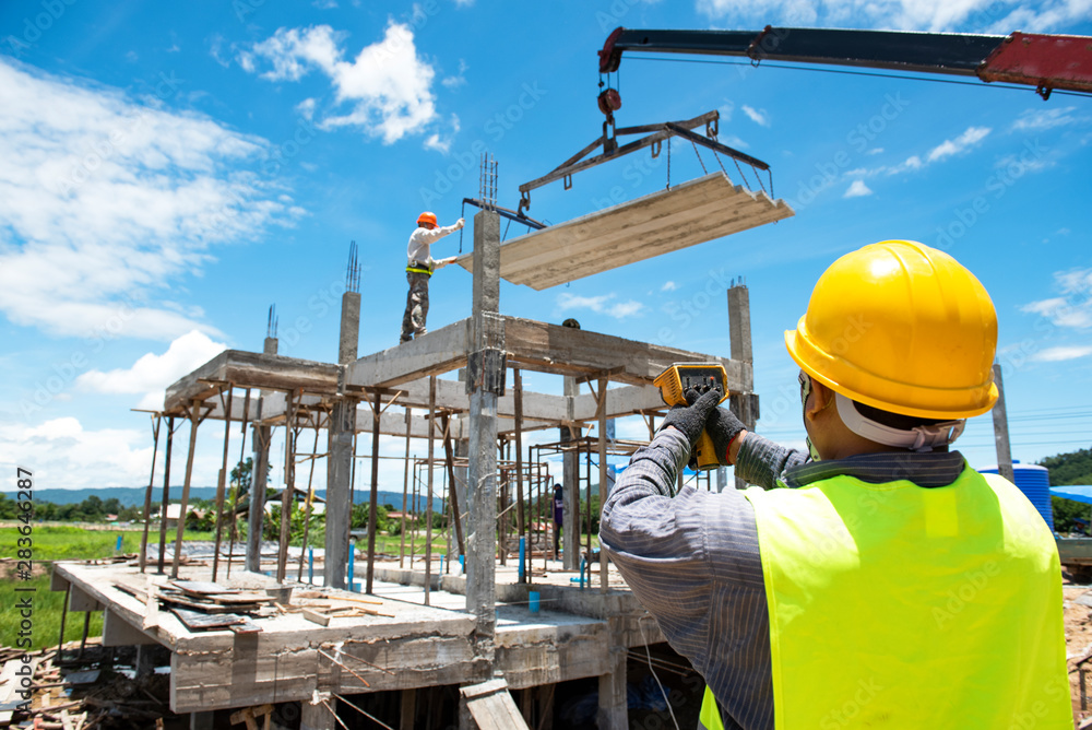 Construction workers control the spread of concrete slabs in the construction area and the bright blue background.