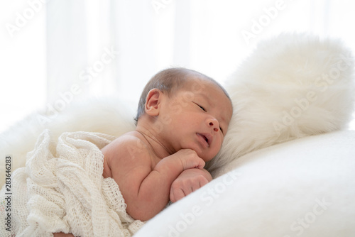 Medium shot 0-1 months beautiful cute asian newborn baby girl infant with black eyes and fragile skin lying down on the soft white baby sleeper blanket photo