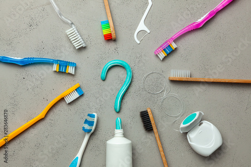 Toothpaste in the form of a question mark and many different and colored toothbrushes and dental floss. Concept of how to choose the right toothbrush or how to brush your teeth
