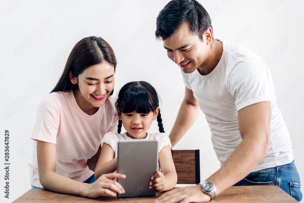 Happy family father and mother with daughter sitting and looking at tablet computer together in the living room at home Happy family father and mother with daughter sitting and looking at tablet computer together in the living room at home