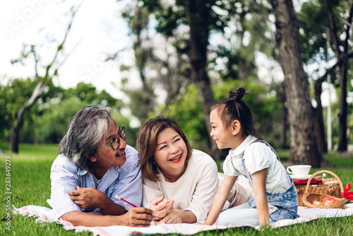 Portrait of happy grandfather with grandmother and little cute girl enjoy relax reading a book in summer park.Young girl with their laughing grandparents smiling together.Family and togetherness