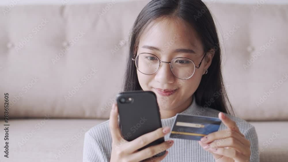 Close-up of Asian women are buying product online with a credit card. Asia girl are sitting using smartphone Via the internet transactions in the living room at home. Close-up of Asian women are buying product online with a credit card. Asia girl are sitting using smartphone Via the internet transactions in the living room at home.