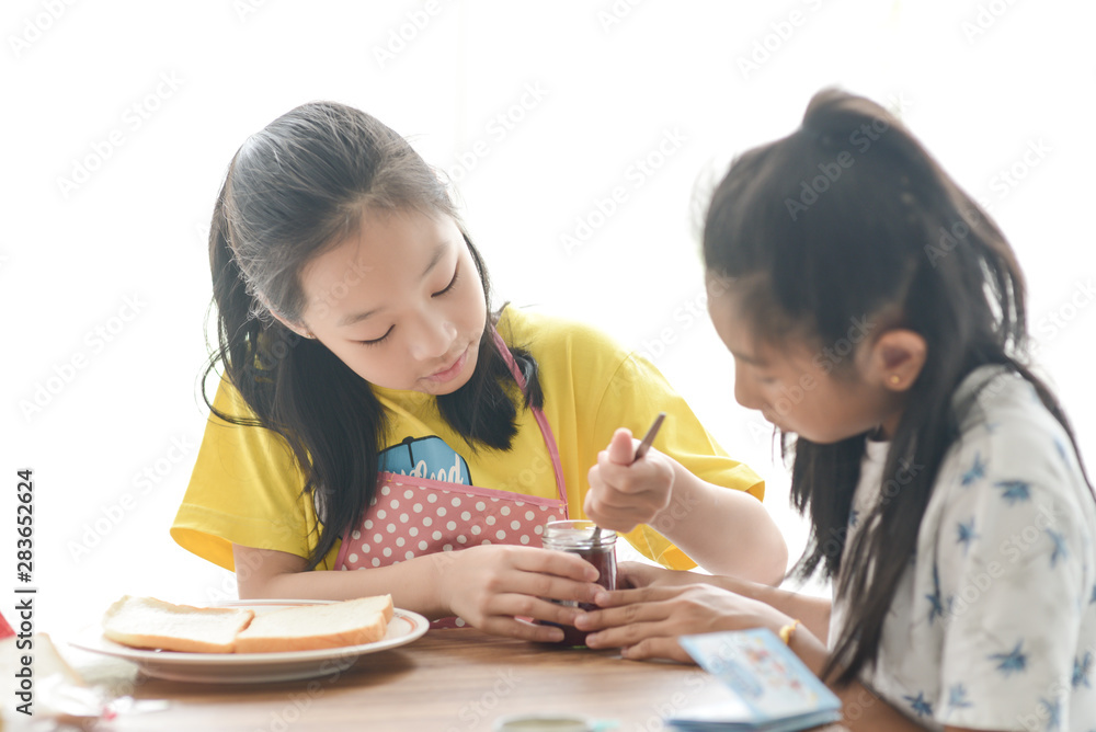 Asian sister spreading strawberry jam on bread for her younger sister, lifestyle concept. Asian sister spreading strawberry jam on bread for her younger sister, lifestyle concept.