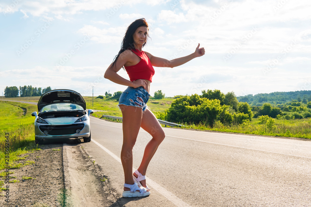 Beautiful woman hitchhiking by a broken car. girl stands at his car and ...