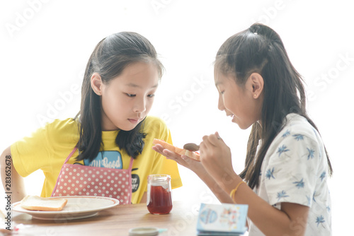 Asian sister spreading strawberry jam on bread for her younger sister, lifestyle concept. photo