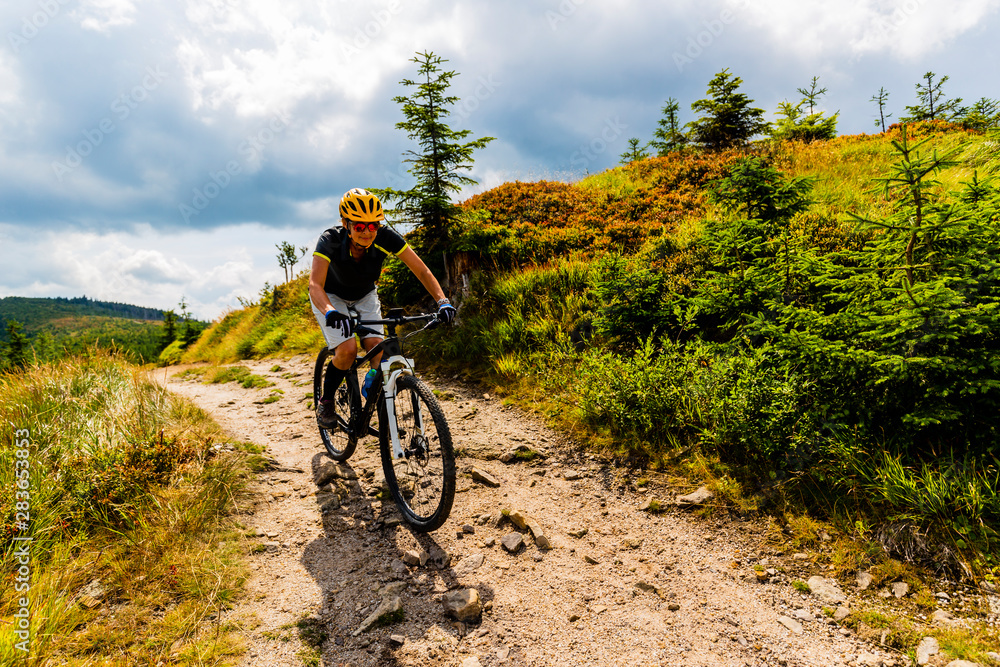 Fototapeta premium Mountain biking woman riding on bike in summer mountains forest landscape. Woman cycling MTB flow trail track. Outdoor sport activity.