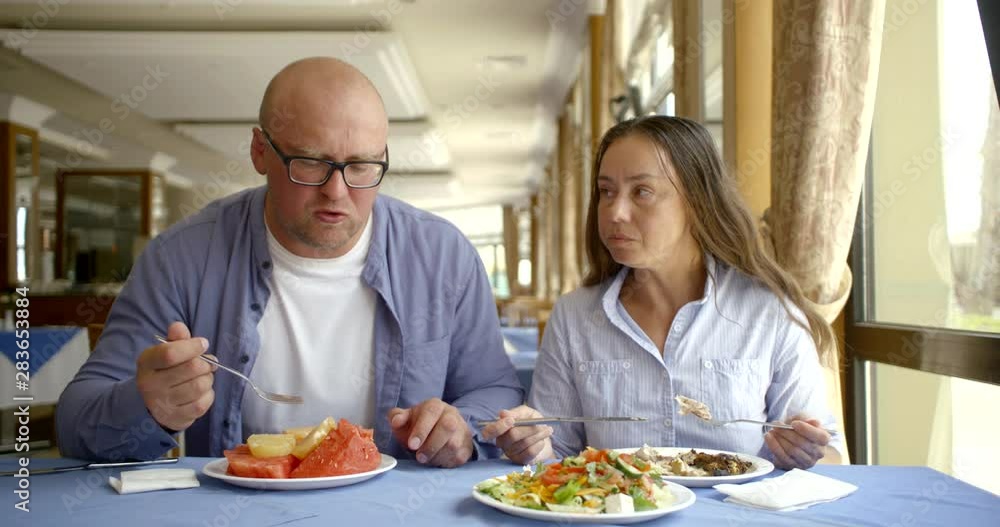 A middle - aged adult couple dine in the restaurant during the day. Man to eat fruits and female fish A middle - aged adult couple dine in the restaurant during the day. Man to eat fruits and female fish