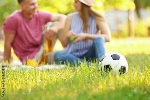 Blurred view of young couple having picnic in sunny summer park, focus on soccer ball