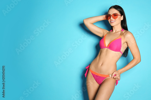Beautiful young woman in stylish bikini with sunglasses on light blue background. Space for text