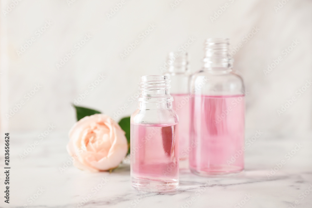 Bottles of essential oil and rose on marble table Bottles of essential oil and rose on marble table