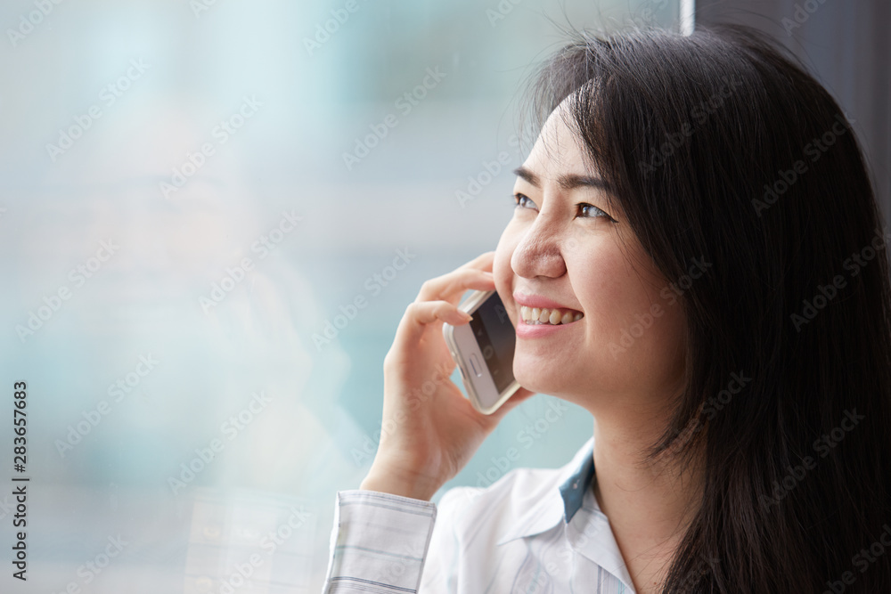 Asian busniness woman Is talking on a mobile phone by the window, there is a fair light the building window. Asian busniness woman Is talking on a mobile phone by the window, there is a fair light the building window.