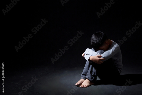 Asian Boy Sitting on Floor and Face Down on knee ISOLATED on Black Background. Concept : Depressed. Disappointed. Emotion.