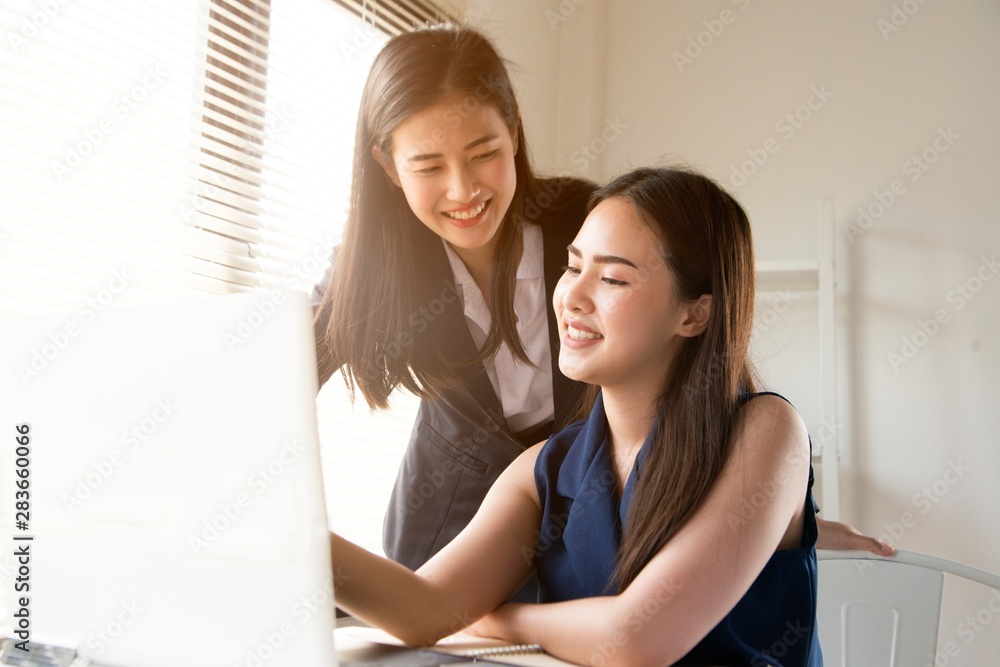 Two young attractive women in business suits are sitting at a desk and discussing workflows is the Head and subordinates. Working team of professionals and colleagues. Two young attractive women in business suits are sitting at a desk and discussing workflows is the Head and subordinates. Working team of professionals and colleagues.