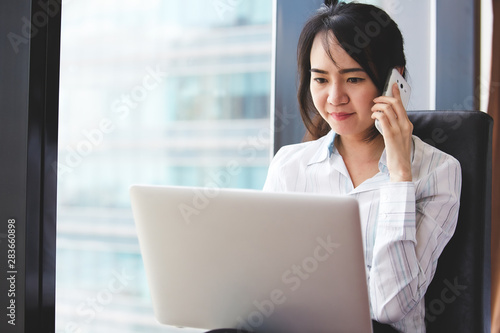 Asian business woman in smile face are using mobile phones and laptops in the office.
