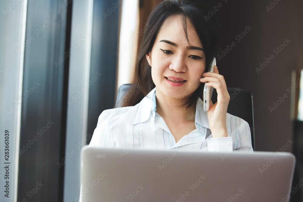 Asian business woman in smile face are using mobile phones and laptops in the office.