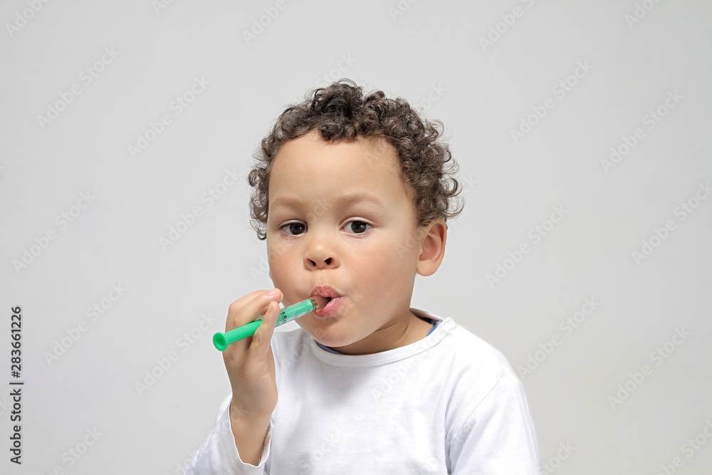 Young boy taking medicine on grey background stock photo Young boy taking medicine on grey background stock photo