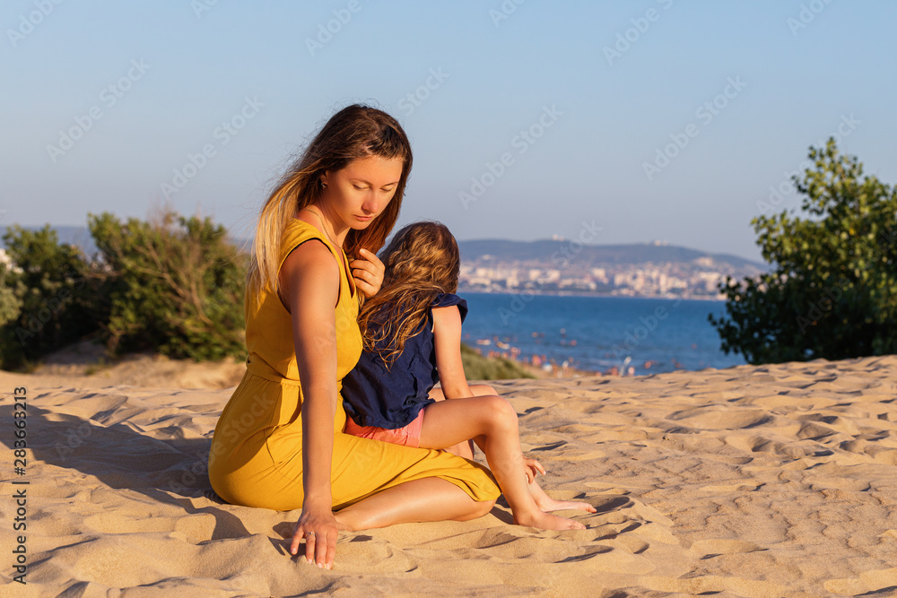 Mom and daughter rest on the sand dunes by the sea. Family Relationship Concept Mom and daughter rest on the sand dunes by the sea. Family Relationship Concept