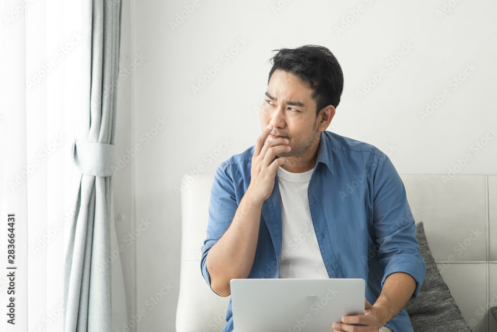 Stressed Asian man using laptop at home, lifestyle concept with copy space.
